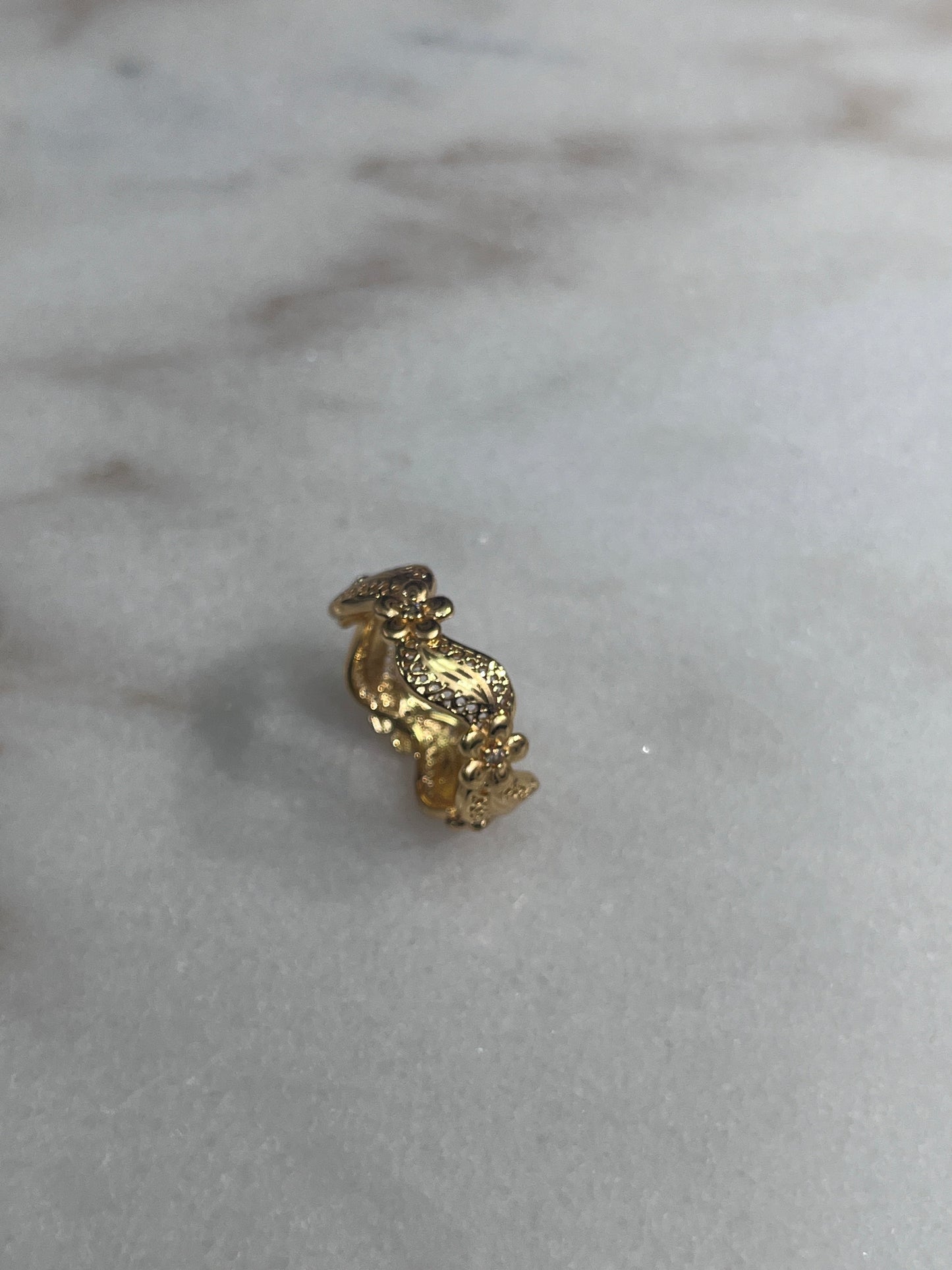 Imitated Gold Curved Ring with Flower Design by Palestinian Elegance on a marble surface