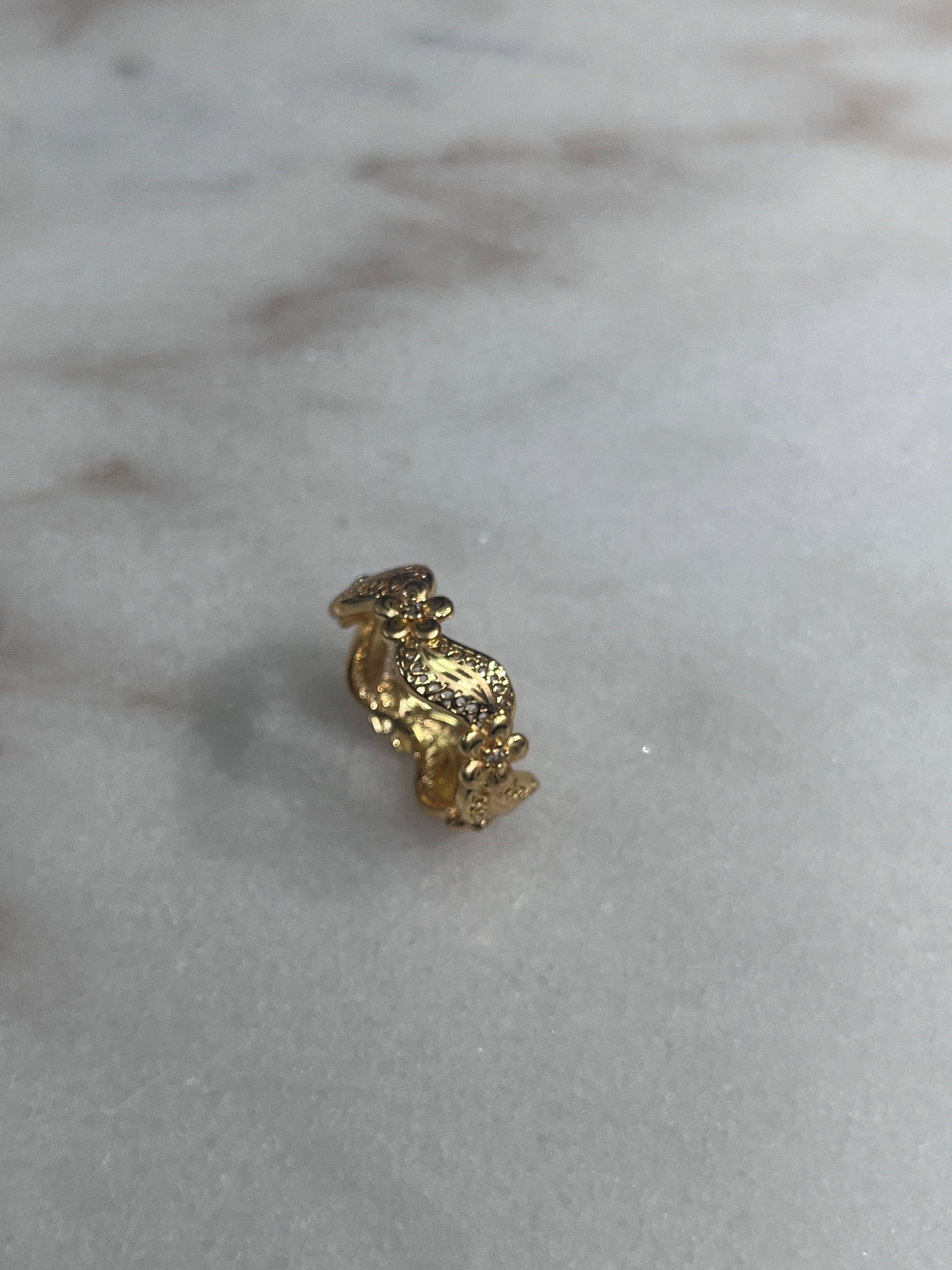 Imitated Gold Curved Ring with Flower Design by Palestinian Elegance on a marble surface