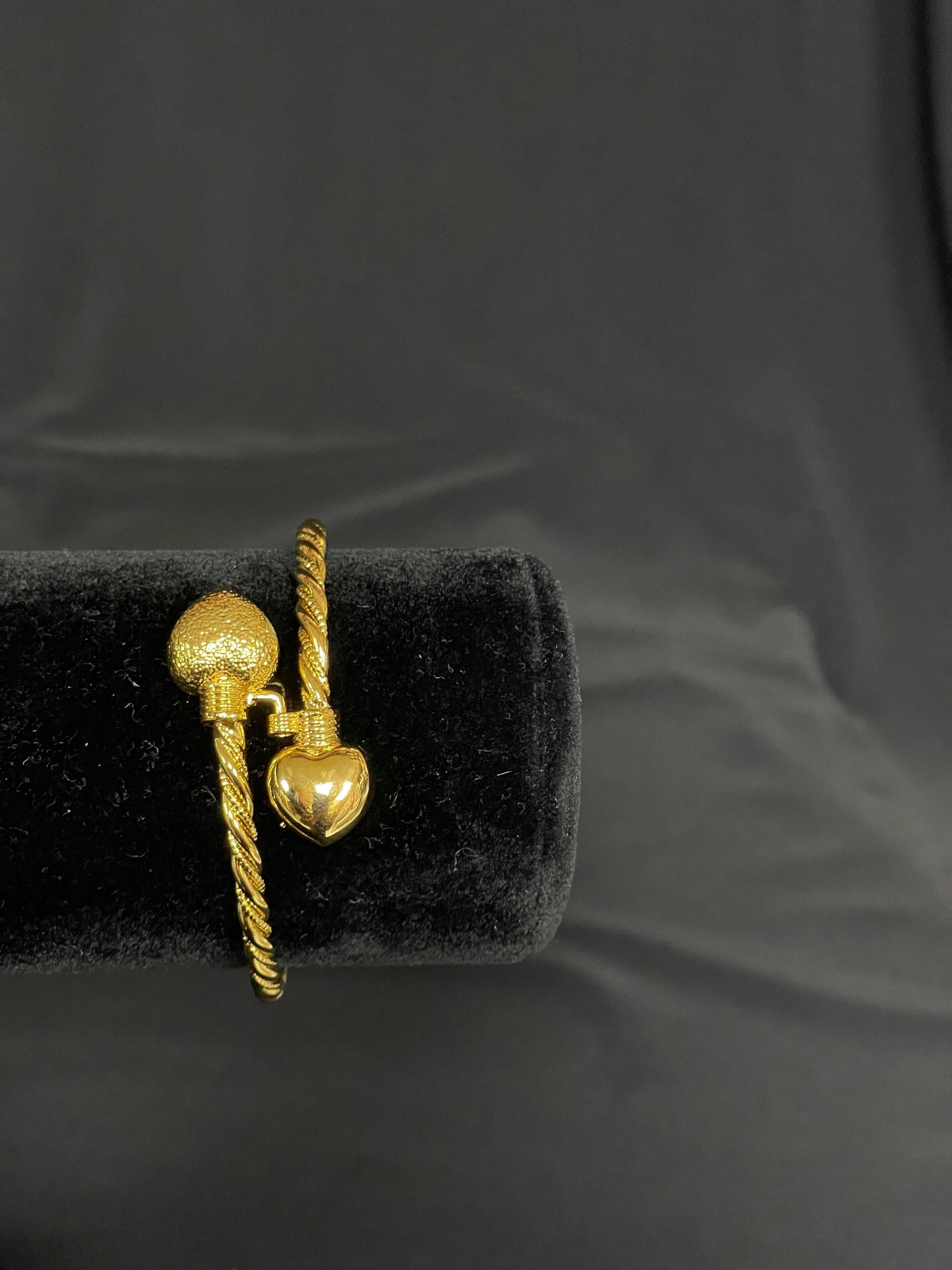 Palestinian Elegance Mabroma Gold Heart Bracelet with twisted band and heart-shaped charms on black display