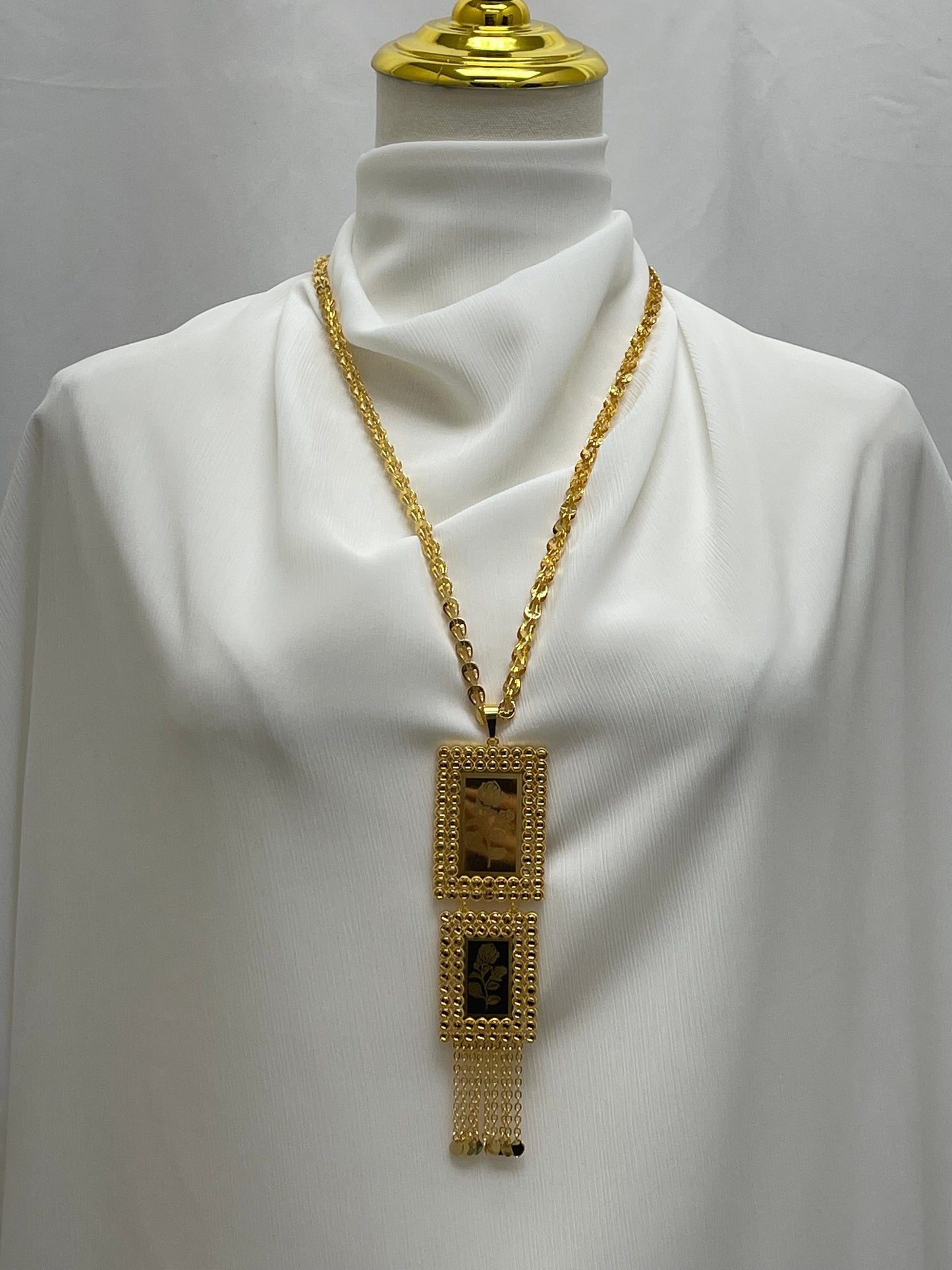 Palestinian embroidered gold necklace with rectangular pendants and chain tassels displayed on white fabric