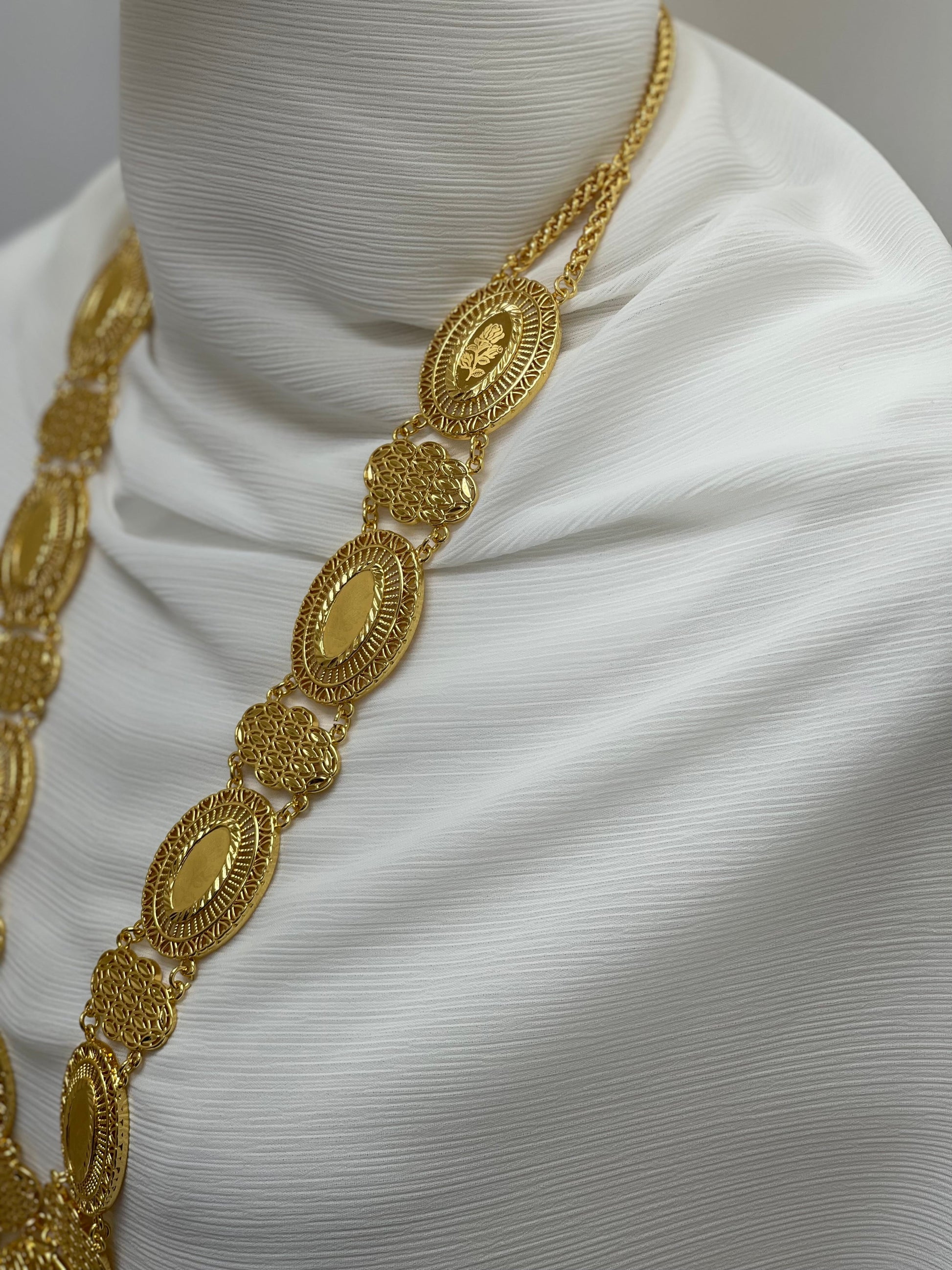 Gold Palestinian embroidered necklace with intricate oval and floral designs displayed on white fabric