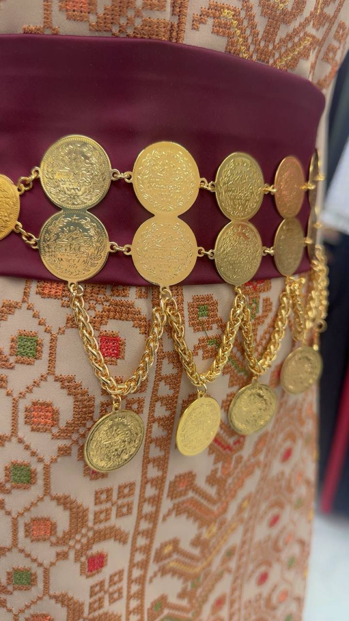 Palestinian Gold Coin-Adorned Zunnar Belt by Palestinian Elegance with intricate gold coins and chains on maroon fabric
