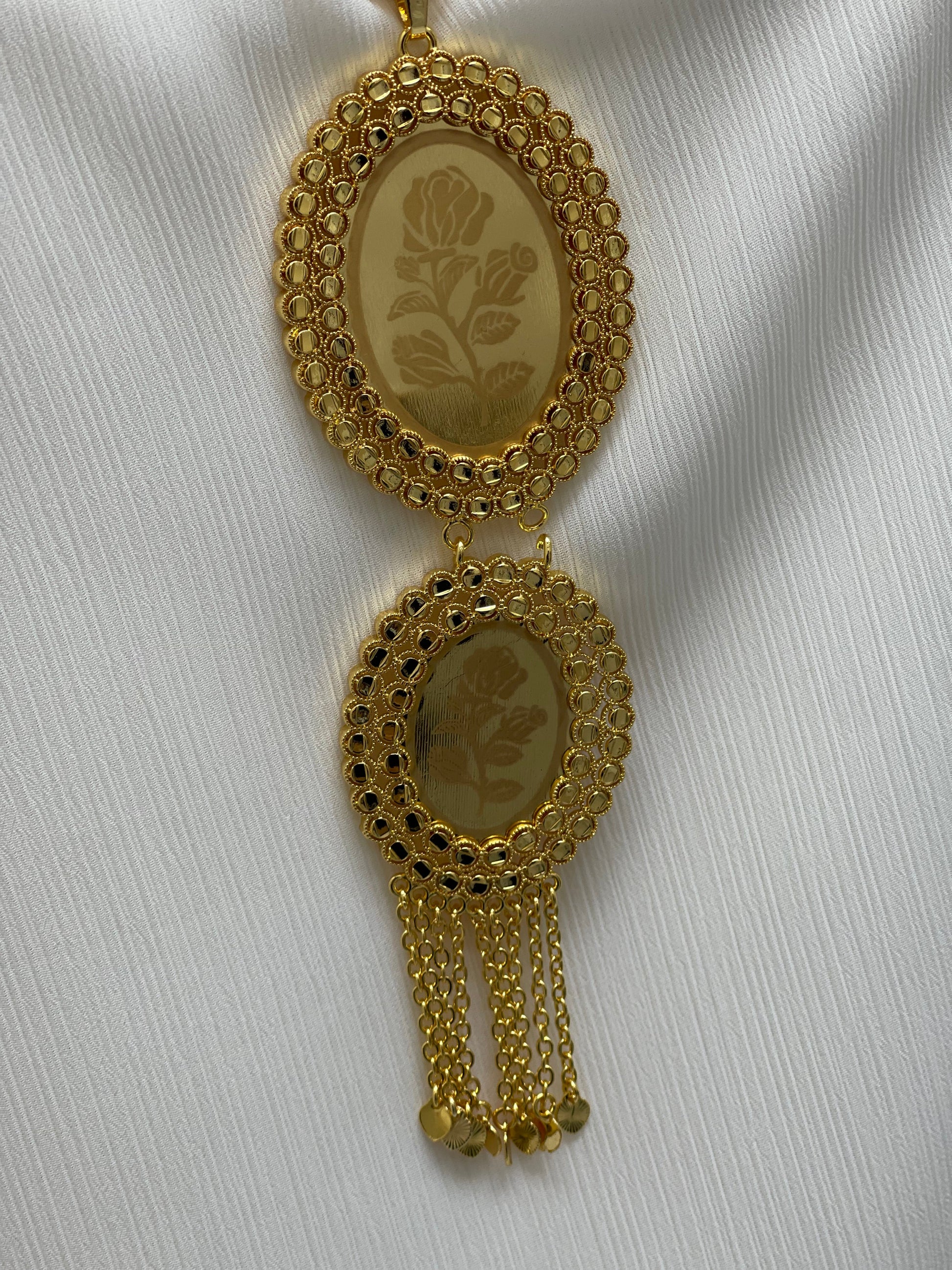 Palestinian Elegance imitated gold oval necklace with floral design and chain tassels on white fabric