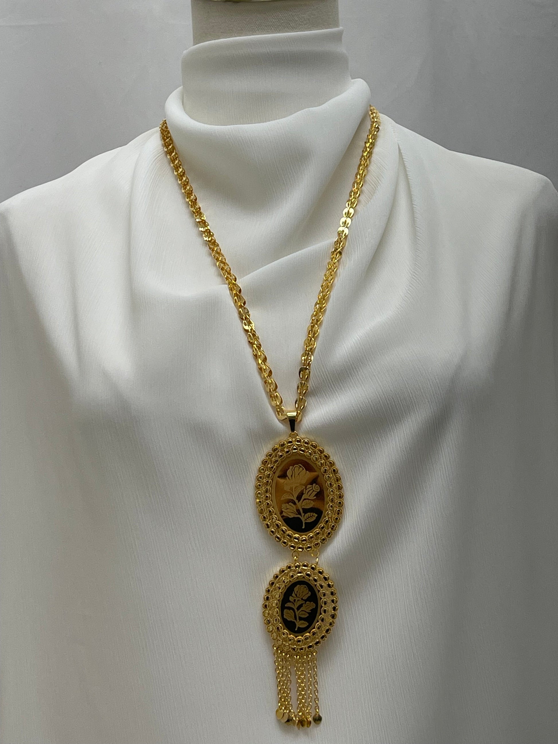 Palestinian Elegance imitated gold oval necklace with floral design and hanging chains on white fabric